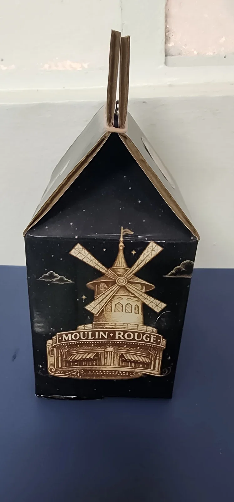 Cara lateral del empaque con ilustración del Moulin Rouge y cierre superior.